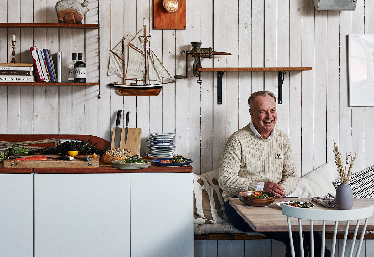 Thomas, ägare av Nordhamn, sitter skrattandes på en långbänk vid ett restaurangbord. Han serveras sashimi och grönsaker. På bänken bredvid bordet står ett knivställ med knivar från Nordhamn, färskt bröd ligger på bänken. En skärbräda i trä där lax, grönsaker skurits upp med kockkniven från Nordhamn.
På väggen hänger en segelbåt, stringhylla och en köttkvarn.